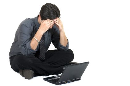 Man sitting on the floor next to a Netbook laptop with his hands on his forehead